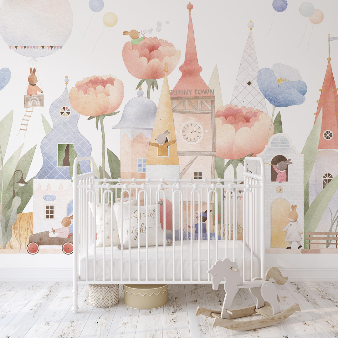Children's room with a crib and decorative wall mural featuring cartoon houses and flowers.