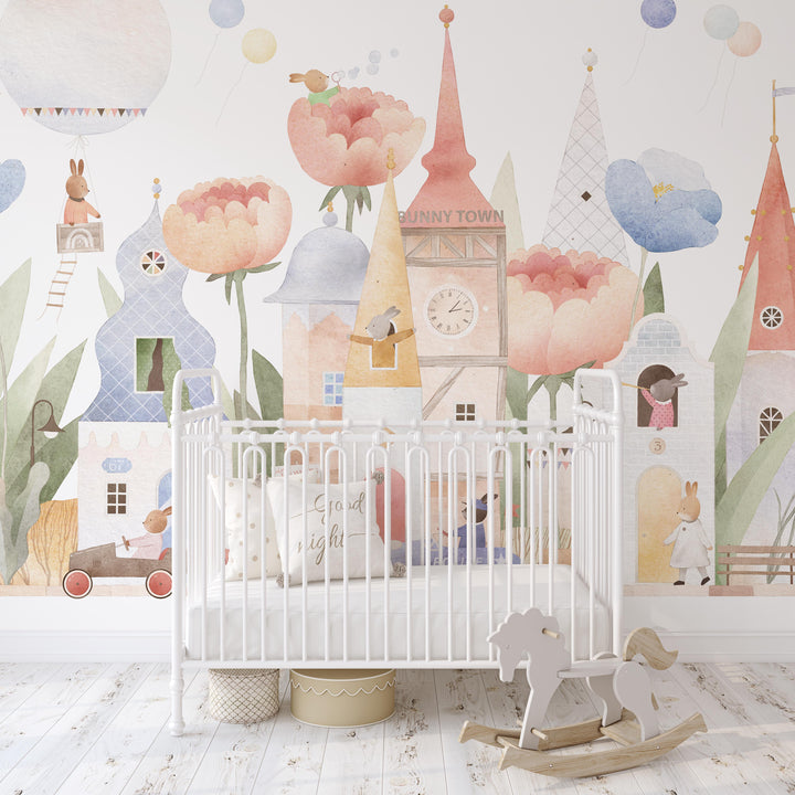 Children's room with a crib and decorative wall mural featuring cartoon houses and flowers.