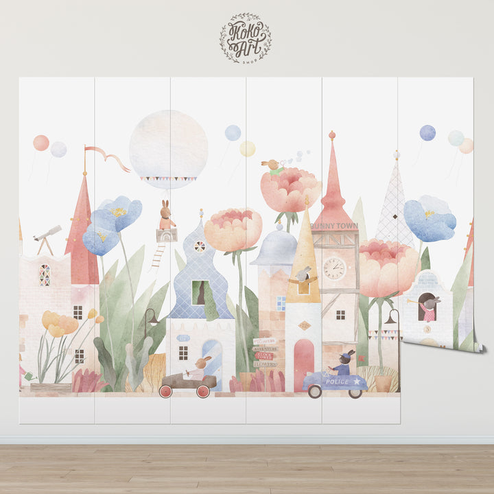 Decorative wall mural with cartoon houses, flowers, and balloons on a white wall.